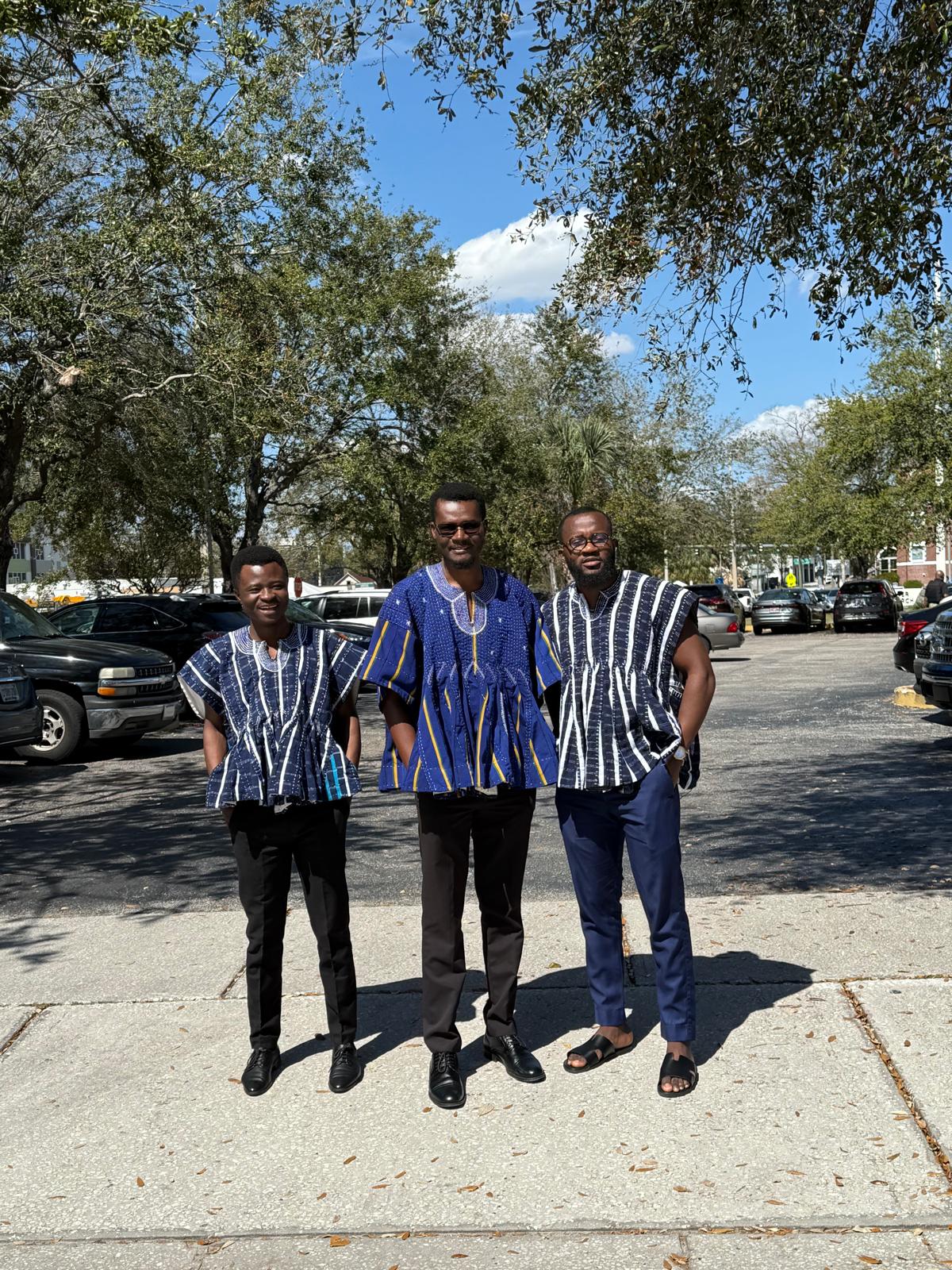 Three men wearing Ghanaian traditional smocks outdoors